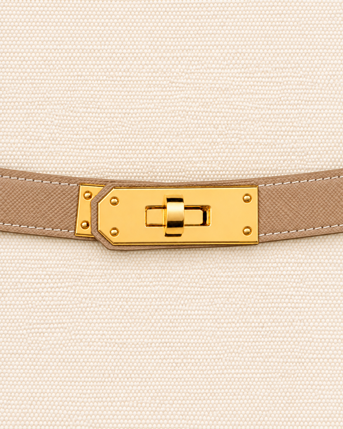 A close-up of a beige textured leather belt with a gold-tone turn-lock clasp, shown against a matching beige woven fabric background. Boat Tote Boatkin bag handbag 