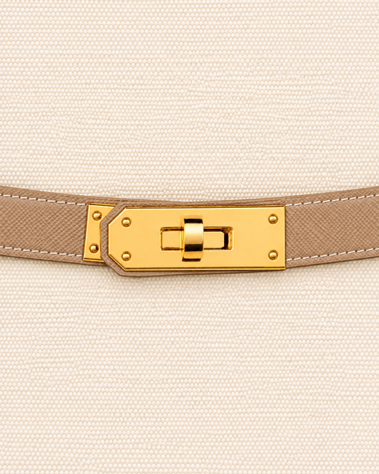 A close-up of a beige textured leather belt with a gold-tone turn-lock clasp, shown against a matching beige woven fabric background. Boat Tote Boatkin bag handbag 