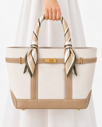A structured tote bag in cream and beige with a striped silk scarf handle, held by a person wearing a white dress against a clean white background. Boat Tote Boatkin bag handbag 