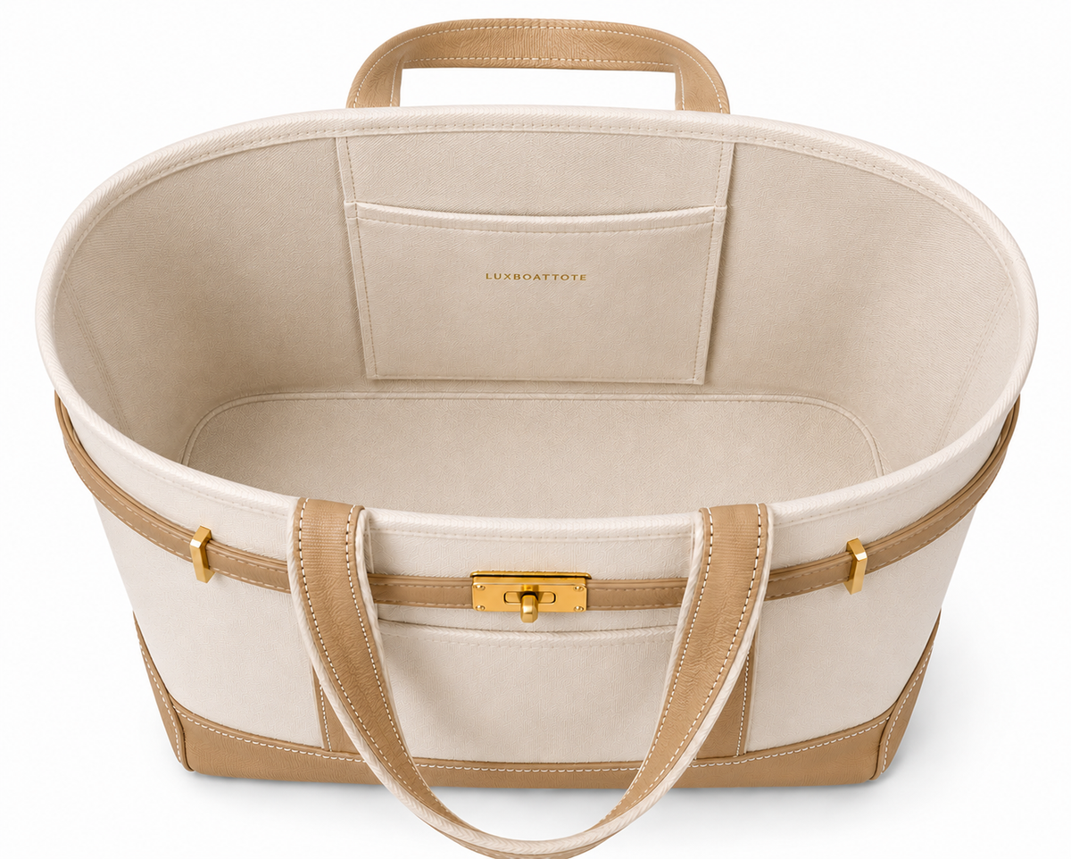 A structured tote bag in cream canvas with tan leather trim, handles, and base, featuring a gold-tone front clasp and a zip-around top.Boat Tote Boatkin bag handbag 