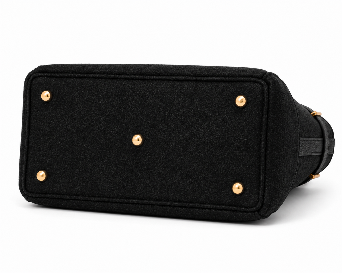 Black felted wool shoulder bag shown from the bottom corner, featuring gold-tone metal studs and a black leather strap on a white background.