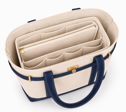 A beige canvas tote bag organizer insert with navy blue handles and trim, featuring gold-tone hardware and multiple interior zip and pocket compartments, shown on a white background.