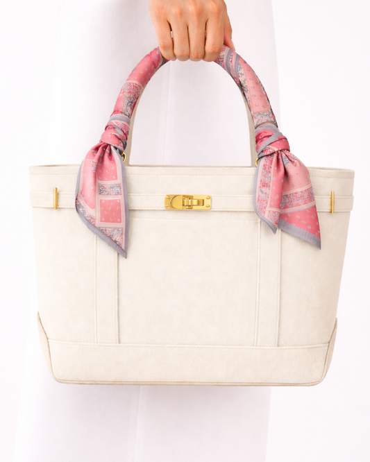 White handbag with a pink and gray checkered scarf held by a hand on a white background