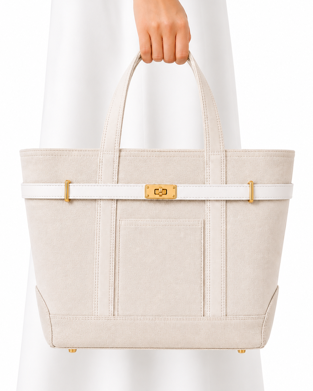 A structured tote bag in light beige textured leather with a white horizontal strap detail and gold-tone hardware, held by a person wearing a white dress against a white background.